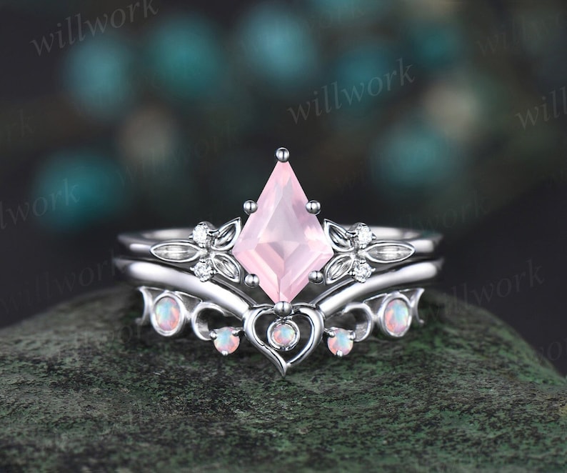 May include: A delicate engagement ring set with a pink gemstone and a heart-shaped design. The ring is set in white gold and features a row of smaller gemstones on the band.