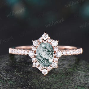 Peut inclure: Une bague de fiançailles en or rose avec une pierre centrale ovale en agate mousse verte entourée d'un halo de petits diamants. La bande est également sertie de petits diamants.