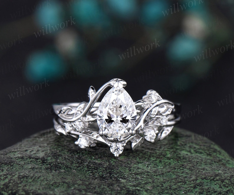 May include: A pear-shaped diamond engagement ring set in a white gold band with a delicate leaf design. The ring is adorned with smaller diamonds on the band and leaves.