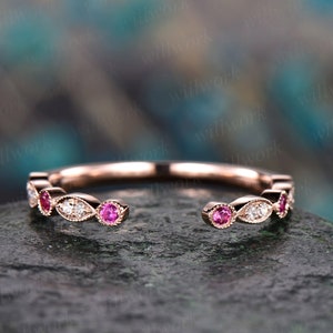 May include: A delicate rose gold band with a row of alternating pink and white gemstones. The band is open on one side, making it a unique and stylish piece of jewelry.