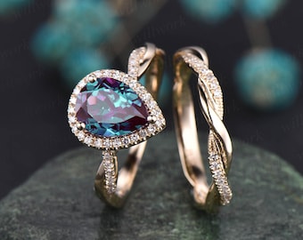 Op de afbeelding: Een ring met een peervormige, iriserende edelsteen die is gezet in een halo van kleinere diamanten. De ring is gemaakt van roségoud en heeft een gedraaide band. De bijpassende trouwring is ook gemaakt van roségoud en heeft een gedraaide band met kleine diamanten.