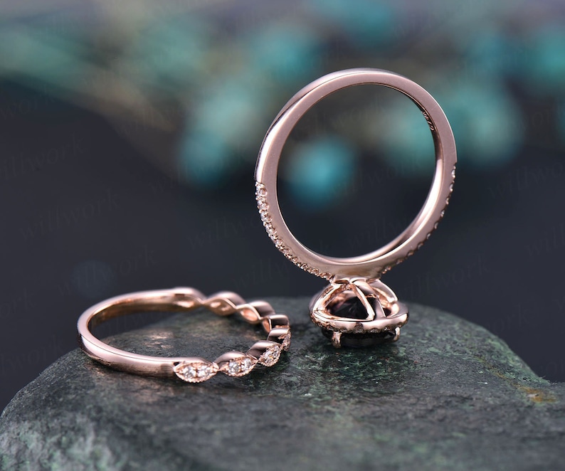 May include: Rose gold engagement ring set with a black centre stone and a halo of smaller stones. The band is encrusted with small accent stones. The matching band features a series of marquise-shaped stones.