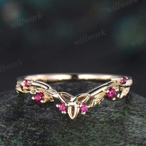 May include: A delicate gold ring with a Celtic knot design and five small ruby stones. The ring is set on a dark background.