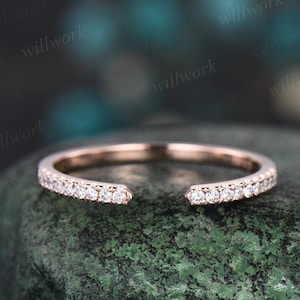 May include: A delicate rose gold band with a row of small diamonds set in a pave setting. The band is open on one side, creating a unique and modern look.