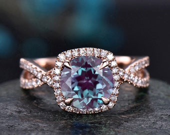 May include: A rose gold engagement ring with a large, square-cut alexandrite gemstone surrounded by a halo of smaller diamonds. The band is a twisted design with smaller diamonds set along the sides.