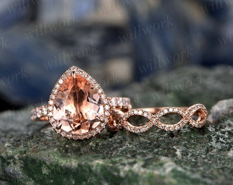 May include: A pear-shaped morganite engagement ring set in rose gold with a halo of diamonds. The set includes a matching wedding band with a delicate diamond-encrusted design.