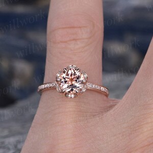 May include: A rose gold engagement ring with a round, light pink center stone surrounded by a halo of smaller diamonds. The band is also set with smaller diamonds.