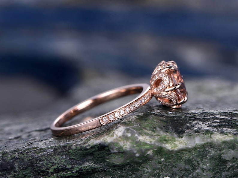 May include: A rose gold engagement ring with a round, light pink gemstone surrounded by smaller diamonds. The band is also set with small diamonds.