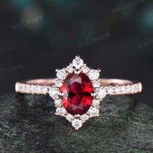 May include: A rose gold engagement ring featuring a large oval ruby surrounded by a halo of smaller diamonds. The band is also set with diamonds.