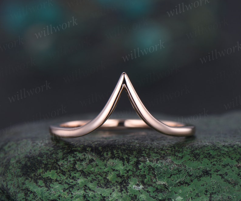 May include: A rose gold wedding band with a V-shaped design. The band is simple and elegant, and would make a beautiful addition to any wedding ensemble.