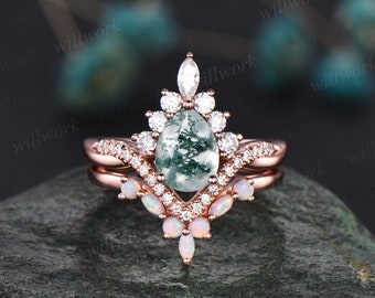 Könnte beinhalten: Verlobungsring-Set aus Roségold mit einem grünen Moosachat-Mittelstück und einem Heiligenschein aus klaren runden Steinen. Die Band ist mit einer Reihe von Opal-Steinen verziert.