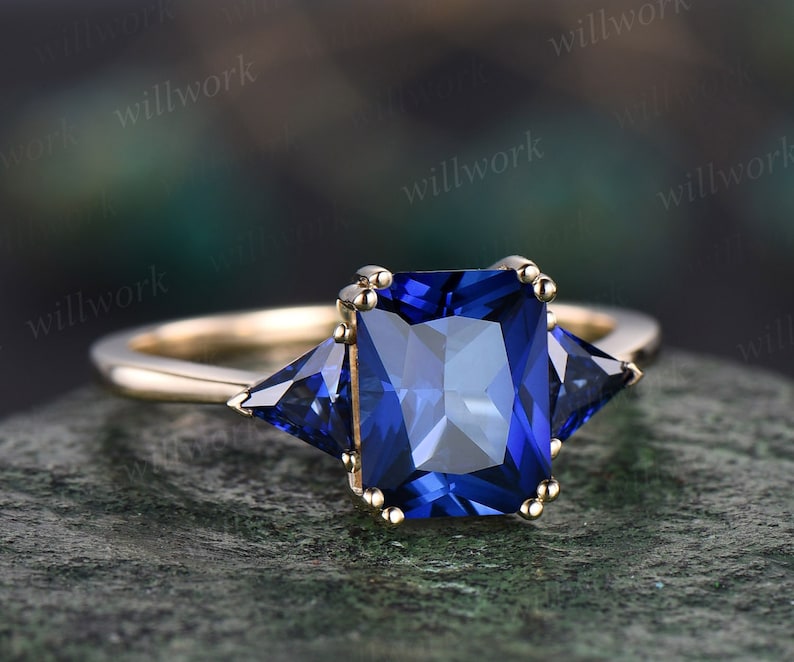 May include: A gold ring with a large square blue sapphire center stone and two smaller triangular blue sapphire accent stones