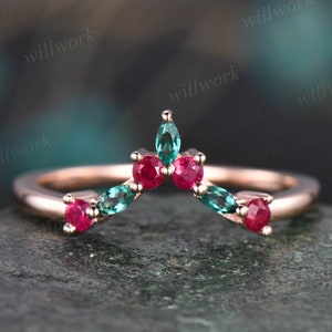 May include: A rose gold ring with a curved design featuring alternating red and green gemstones. The ring is set with emerald cut gemstones.