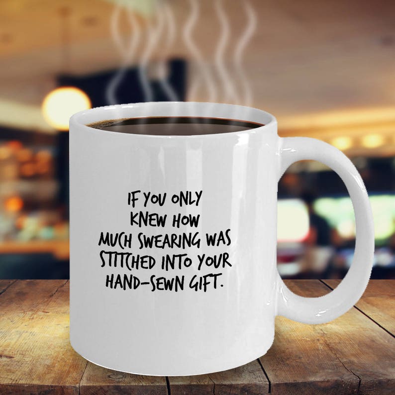May include: White ceramic coffee mug with black text that reads "If you only knew how much swearing was stitched into your hand-sewn gift."