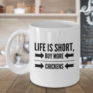 May include: White ceramic coffee mug with black text that reads "Life is short, buy more chickens" with arrows pointing to the left and right of the text.