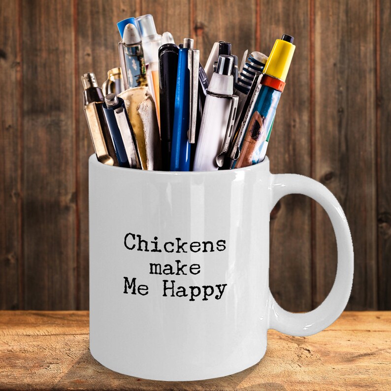 May include: White ceramic mug with a black inscription that reads "Chickens make me happy". The mug is filled with a variety of pens and pencils.