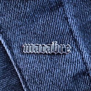 May include: Silver pin with the word "macabre" in a gothic font.