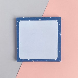 May include: A blue notepad with a white border and white stars. The notepad is on a pink and grey background.