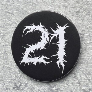 May include: A black and white round sticker with the number 21 in a stylized font. The number is white and the background is black.