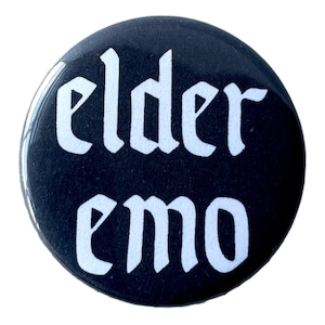 Può includere: Bottone nero con testo bianco che recita "elder emo" in un font gotico.