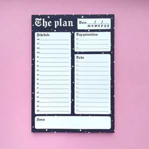 Può includere: Un planner nero e bianco con un design a cielo stellato. Il planner ha sezioni per "The Plan", "Schedule", "Top Priorities", "Todo" e "Notes".