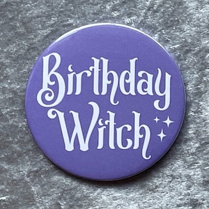 Op de afbeelding: Ronde paarse knop met witte tekst die "Birthday Witch" zegt met twee witte sterren.