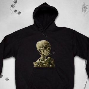May include: Black hooded sweatshirt with a graphic print of a skeleton smoking a pipe. The skeleton is in a seated pose and is wearing a hat. The graphic is in a painterly style.