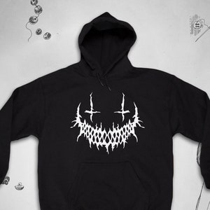 May include: Black hooded sweatshirt with a white graphic of a stylised smiling face with two crosses above it.