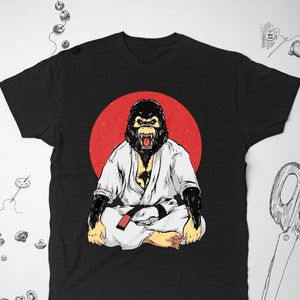 May include: Black t-shirt featuring a graphic of a gorilla wearing a white karate gi and a red belt, sitting in a meditative pose against a red circle.