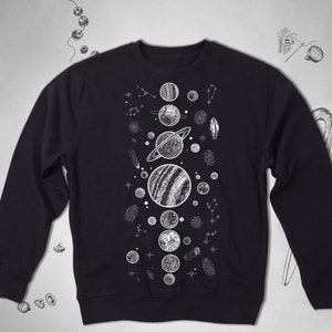 Peut inclure: Sweat-shirt noir avec un imprim&eacute; graphique blanc de plan&egrave;tes et d'&eacute;toiles. Le graphique est centr&eacute; sur le devant du sweat-shirt.