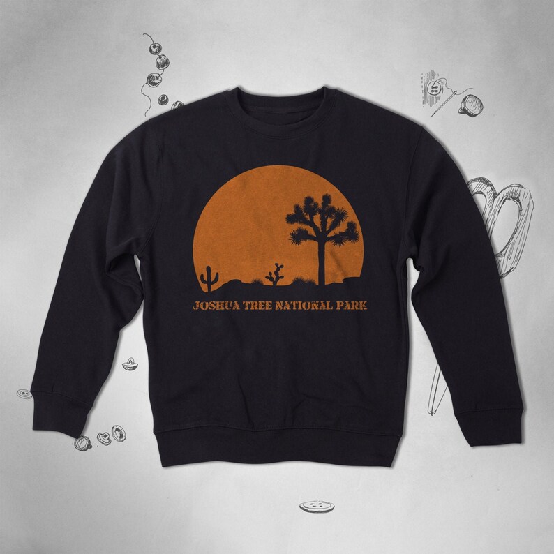 Peut inclure: Sweat-shirt noir avec un graphique repr&eacute;sentant un coucher de soleil dans le parc national de Joshua Tree avec une silhouette d'un Joshua Tree et de cactus. Le texte "Joshua Tree National Park" est imprim&eacute; sous le graphique.