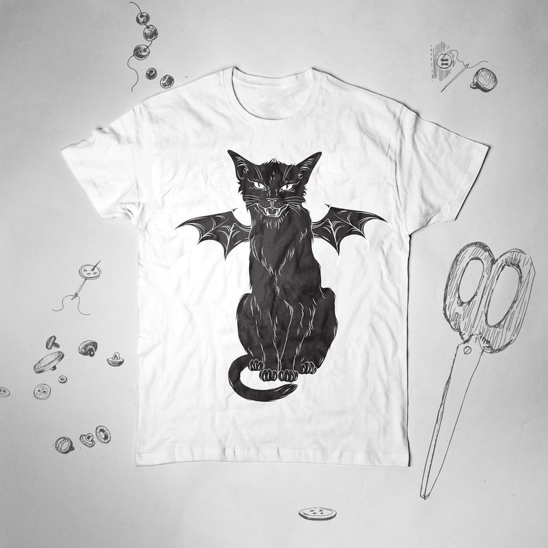 May include: White t-shirt featuring a black cat with bat wings. The cat has an angry expression. The design is a graphic illustration. The shirt is a short-sleeved crew neck.