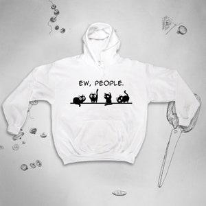 以下が含まれることがあります： 前面に「EW, PEOPLE.」という文字がプリントされた白いフード付きスウェットシャツ。4匹の黒い漫画の猫がテキストの下に並んでいます。