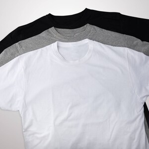 May include: Three t-shirts stacked on top of each other. The top shirt is black, the middle shirt is gray, and the bottom shirt is white.