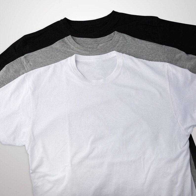 May include: Three t-shirts stacked on top of each other. The top shirt is black, the middle shirt is gray, and the bottom shirt is white.