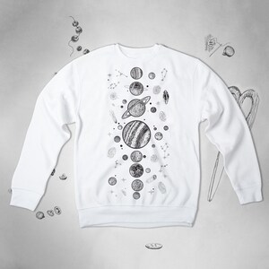 Peut inclure: Sweat-shirt blanc avec un imprim&eacute; graphique noir et blanc de plan&egrave;tes et d'&eacute;toiles. Le graphique est centr&eacute; sur le devant du sweat-shirt.