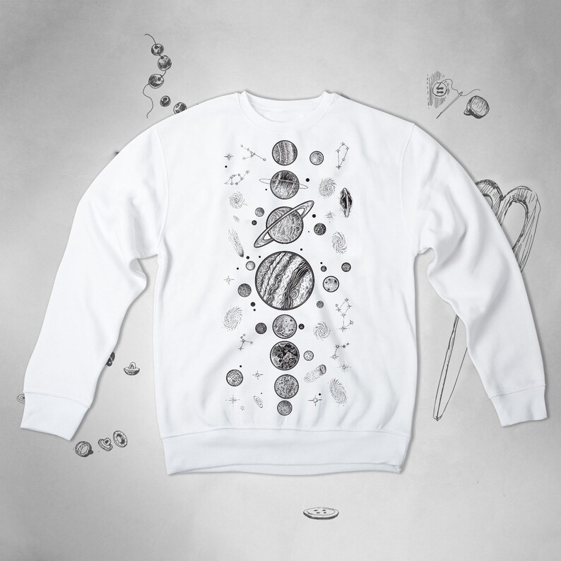 Peut inclure: Sweat-shirt blanc avec un imprim&eacute; graphique noir et blanc de plan&egrave;tes et d'&eacute;toiles. Le graphique est centr&eacute; sur le devant du sweat-shirt.
