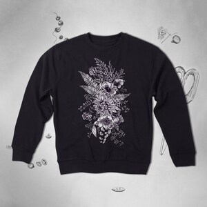 Puede incluir: Una sudadera negra con un estampado floral blanco de un ramo de flores y helechos.