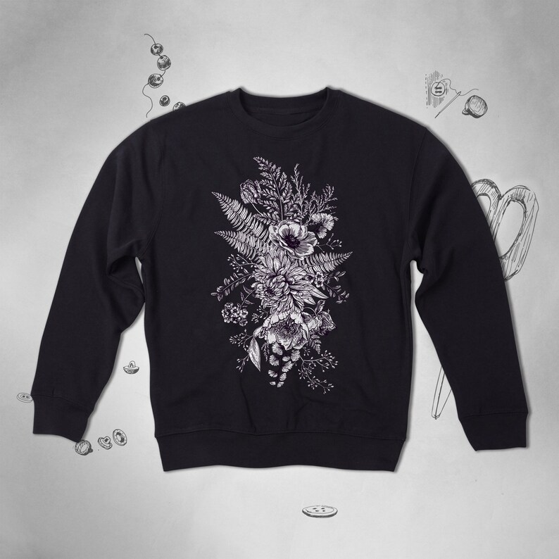 Puede incluir: Una sudadera negra con un estampado floral blanco de un ramo de flores y helechos.
