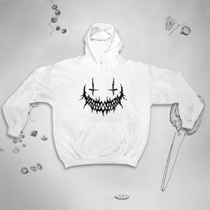 May include: White hooded sweatshirt with a black graphic of a stylised, toothy grin with two crosses above it.