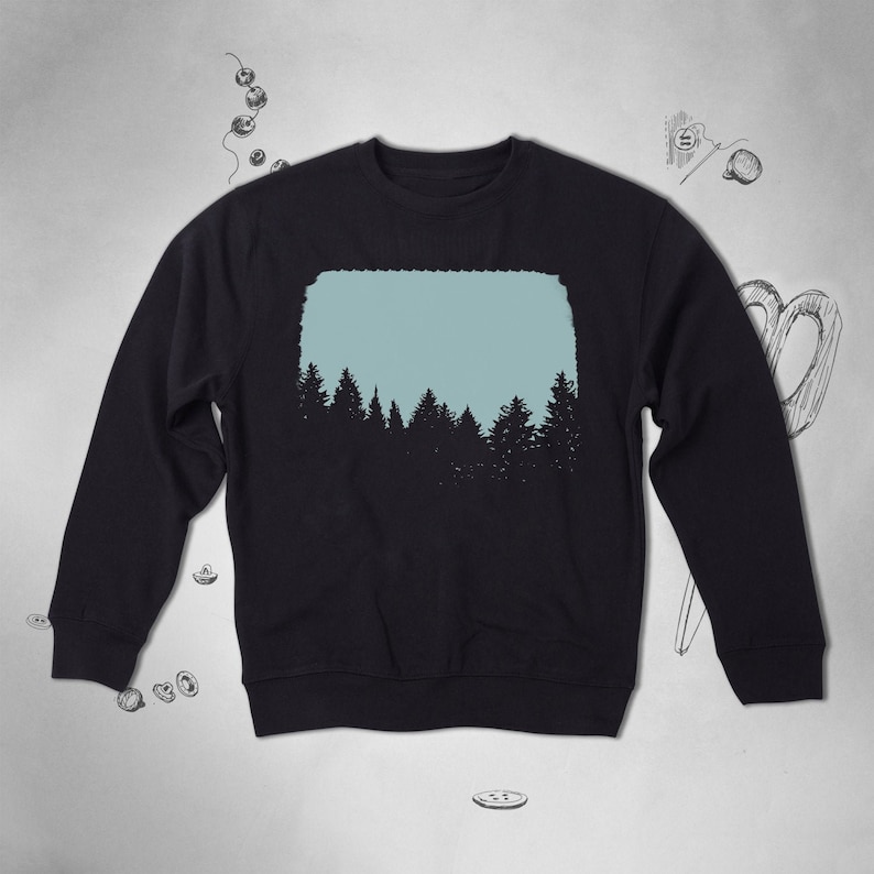 Pu&ograve; includere: Una felpa nera con una grafica di una silhouette di un bosco su uno sfondo blu chiaro.