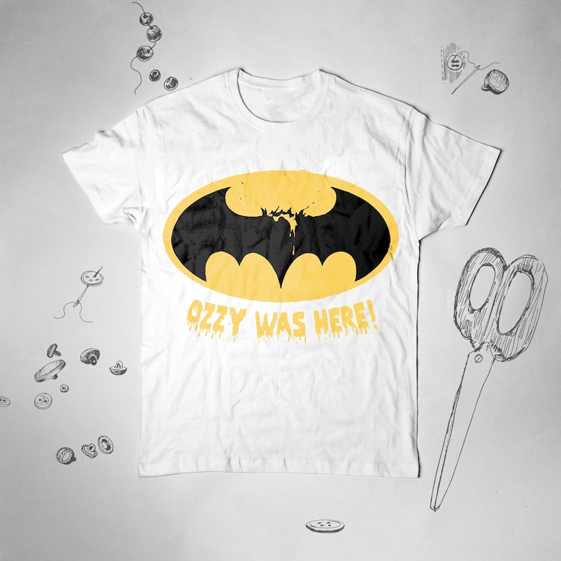 May include: White t-shirt with a yellow Batman logo and the text "Ozzy Was Here!" in dripping yellow letters.