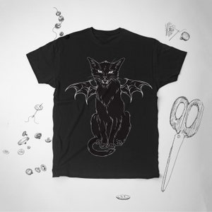 May include: Black t-shirt featuring a white illustration of a cat with bat wings. The cat is sitting upright with an angry expression. The design is a detailed line drawing. The shirt is a crew neck style.