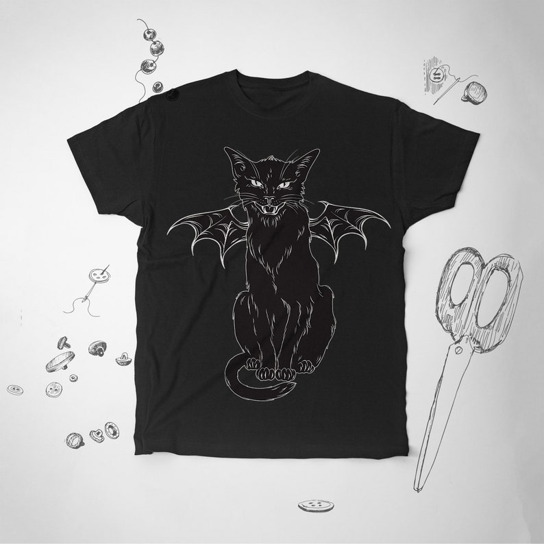 May include: Black t-shirt featuring a white illustration of a cat with bat wings. The cat is sitting upright with an angry expression. The design is a detailed line drawing. The shirt is a crew neck style.