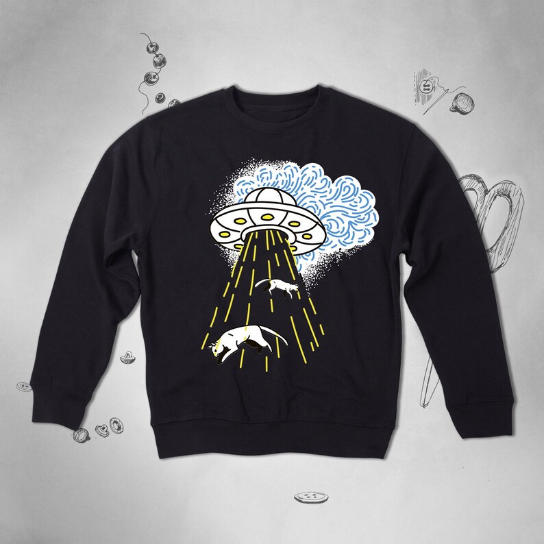 May include: A black sweatshirt featuring a graphic of a UFO beaming up three white cats. The UFO is white with a blue and white cloud behind it.