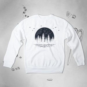 May include: White sweatshirt with a black and white graphic print of a forest silhouette with a full moon and stars. The graphic is centered on the front of the sweatshirt.