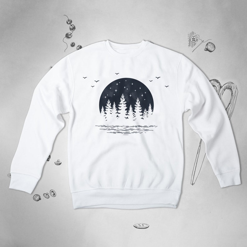 May include: White sweatshirt with a black and white graphic print of a forest silhouette with a full moon and stars. The graphic is centered on the front of the sweatshirt.