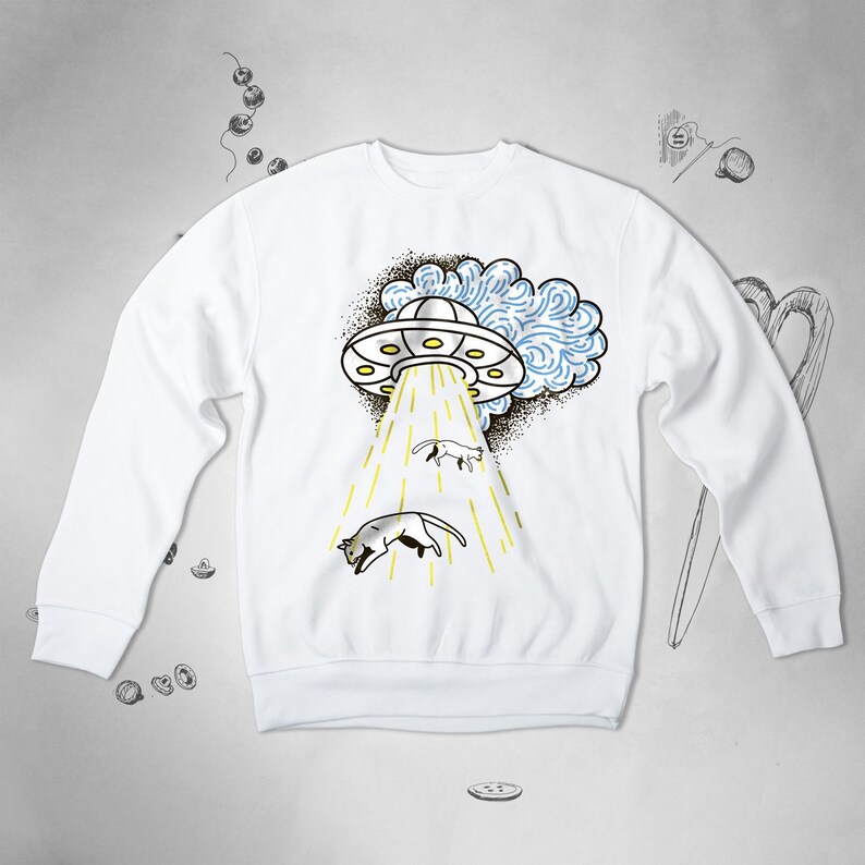May include: White sweatshirt featuring a graphic of a UFO beaming up two cats. The UFO is white with a blue and white cloud behind it. The cats are white with black markings.