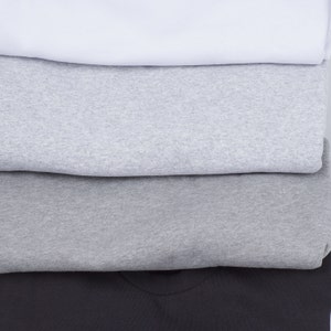 May include: A stack of four t-shirts in different shades of gray and black. The top shirt is white, the second is light gray, the third is a darker gray, and the bottom shirt is black.