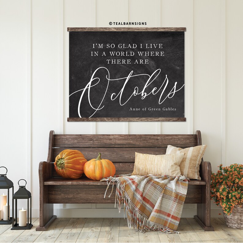 May include: A wooden bench with two orange pumpkins, pillows, and a plaid blanket. Above the bench is a chalkboard sign with the text "I'M SO GLAD I LIVE IN A WORLD WHERE THERE ARE Octobers" and "Anne of Green Gables."